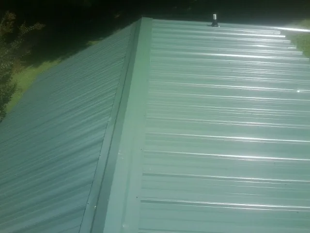 New green metal panels meeting at the ridge of a roof — Flat Roof Repair work by our crew in Wilkes Barre