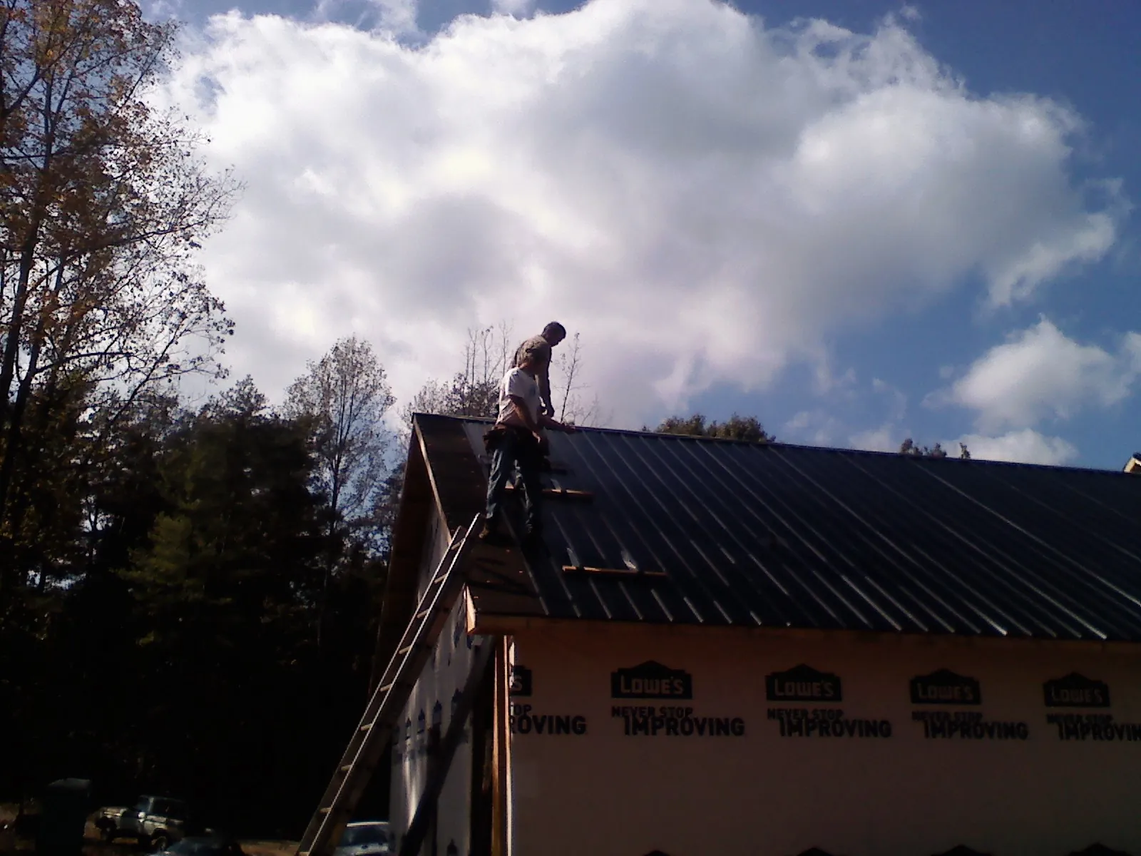 Roofer fastening dark metal panels high against a cloudy sky, from a Roof Inspection job in Wilkes Barre