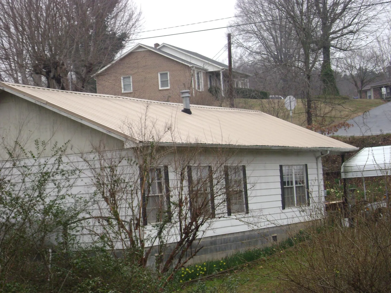 Tan metal roof on a white sided house set into a hillside — Commercial Roofing by Roofing Brothers in Wilkes Barre